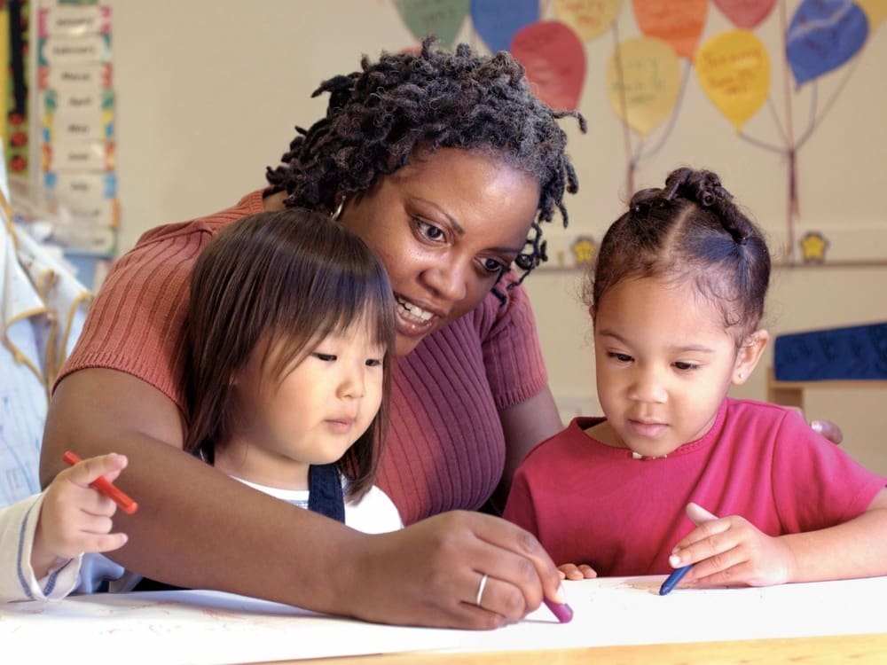 A woman and two children are drawing on paper.